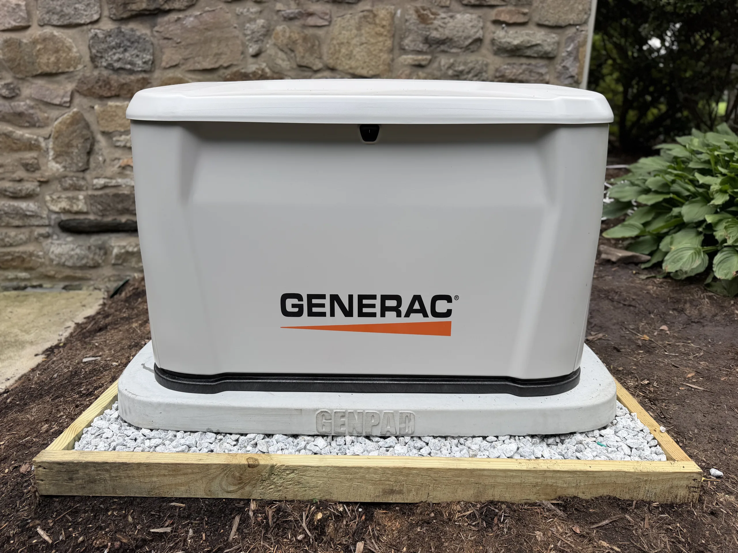 Generac standby generator installed on a gravel pad next to a house
